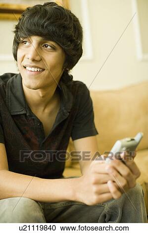 Stock Image - Teenage boy sitting on a couch and smiling. Fotosearch