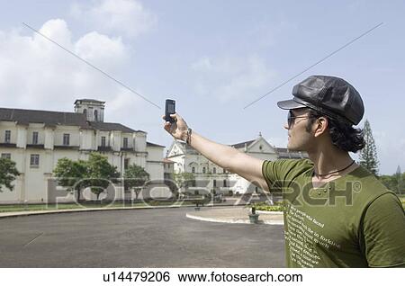 Young man taking a picture of a cathedral with a mobile phone, Se Cathedral, Goa, India View Large Photo Image Stock Photograph - Young man taking a picture of a cathedral with a mobile phone, Se Cathedral, Goa, India. Fotosearch