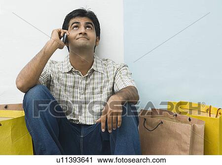 Stock Image - Young man talking on a mobile phone and looking up. Fotosearch