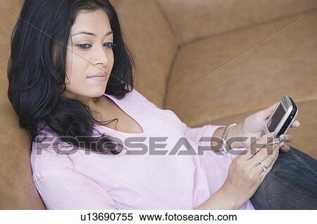 Young woman sitting on a couch and holding a mobile phone View Large Photo Image Stock Photography - Young woman sitting on a couch and holding a mobile phone. Fotosearch