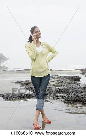 Young woman standing on the beach and talking on a mobile phone View Large Photo Image Stock Image - Young woman standing on the beach and talking on a mobile phone. Fotosearch