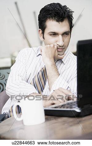 Businessman using a laptop in a restaurant View Large Photo Image Stock Image - Businessman using a laptop in a restaurant. Fotosearch