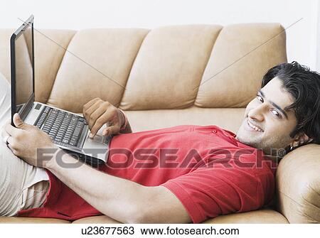 Portrait of a young man lying on a couch and using a laptop View Large Photo Image Stock Image - Portrait of a young man lying on a couch and using a laptop. Fotosearch