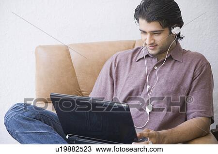 Young man sitting in an armchair and using a laptop View Large Photo Image Stock Image - Young man sitting in an armchair and using a laptop. Fotosearch