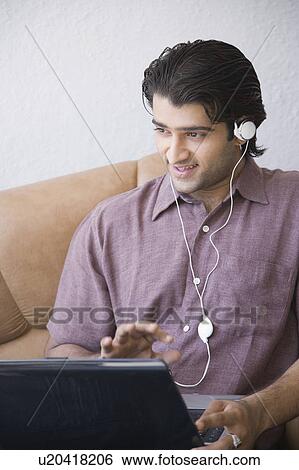 Stock Photograph - Young man sitting in an armchair and using a laptop. Fotosearch