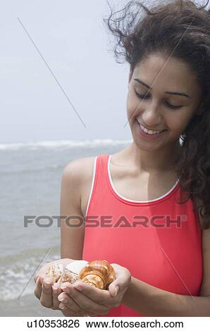 Stock Photograph - Close-up of a young woman holding seashells on the beach and smiling. Fotosearch