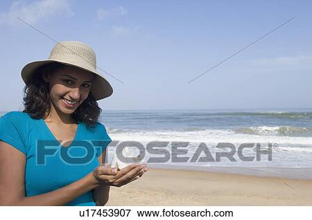 Stock Photo - Portrait of a young woman holding a shell and smiling. Fotosearch