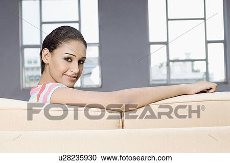 Portrait of a young woman sitting on a couch and smirking View Large Photo Image Stock Image - Portrait of a young woman sitting on a couch and smirking. Fotosearch