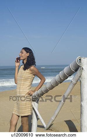 Side profile of a young woman talking on a mobile phone on the beach View Large Photo Image Stock Image - Side profile of a young woman talking on a mobile phone on the beach. Fotosearch