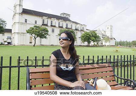 Young woman sitting on a bench with a cathedral in the background, Se Cathedral, Goa, India View Large Photo Image Stock Photo - Young woman sitting on a bench with a cathedral in the background, Se Cathedral, Goa, India. Fotosearch