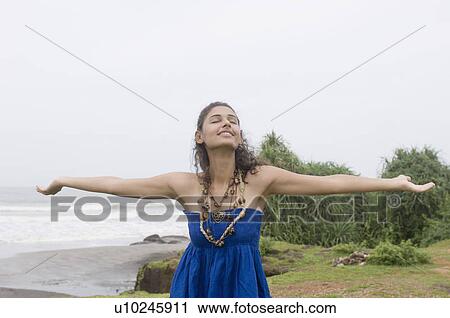 Young woman standing on the beach with her arms outstretched View Large Photo Image Stock Image - Young woman standing on the beach with her arms outstretched. Fotosearch