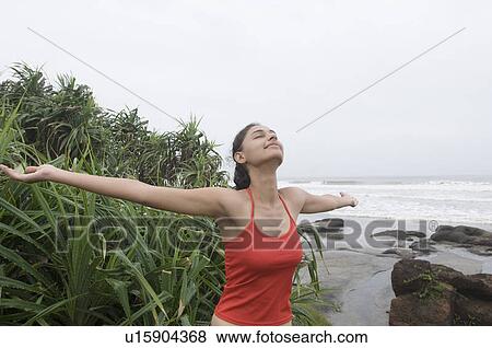 Young woman standing on the beach with her arms outstretched View Large Photo Image Stock Photo - Young woman standing on the beach with her arms outstretched. Fotosearch