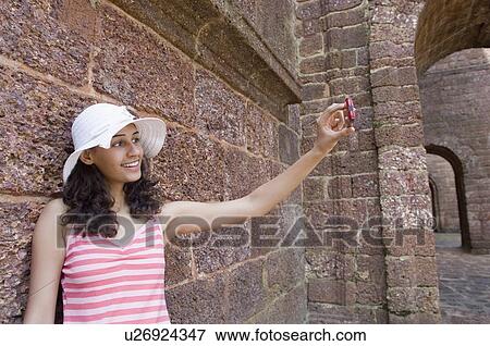 Young woman talking a photograph with a mobile phone and smiling, Goa, India View Large Photo Image Stock Photo - Young woman talking a photograph with a mobile phone and smiling, Goa, India. Fotosearch