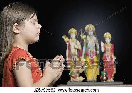 Stock Image - Side profile of a girl praying in front of a Hindu idol. Fotosearch