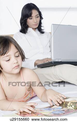 Close-up of a girl watching a magazine with her mother working on a laptop View Large Photo Image Stock Image - Close-up of a girl watching a magazine with her mother working on a laptop. Fotosearch