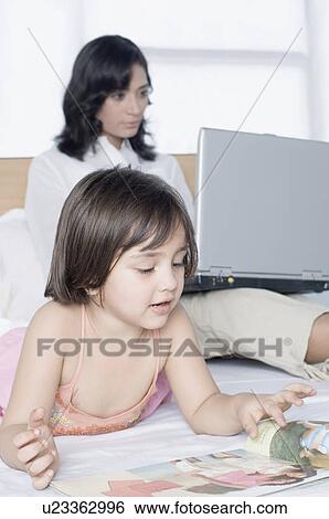 Close-up of a girl watching a magazine with her mother working on a laptop View Large Photo Image Stock Photograph - Close-up of a girl watching a magazine with her mother working on a laptop. Fotosearch
