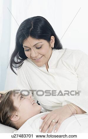 Close-up of a mid adult woman reclining beside her daughter on the bed and smiling View Large Photo Image Stock Image - Close-up of a mid adult woman reclining beside her daughter on the bed and smiling. Fotosearch