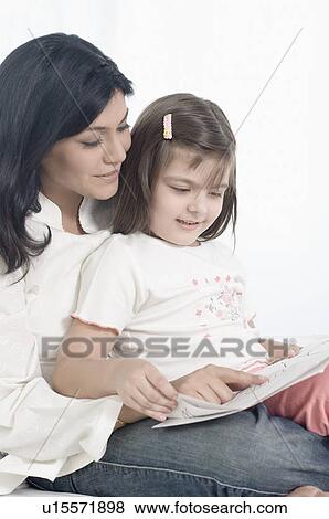 Stock Photo - Close-up of a mid adult woman with her daughter reading a book. Fotosearch