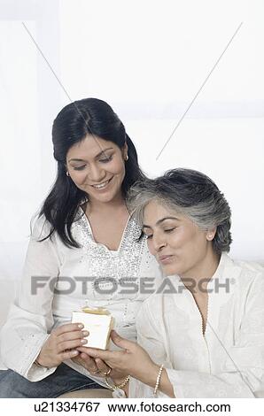 Stock Photo - Mid adult woman giving a gift to her mother on mother's day. Fotosearch
