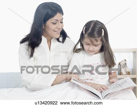 Stock Image - Mid adult woman reading a book with her daughter. Fotosearch