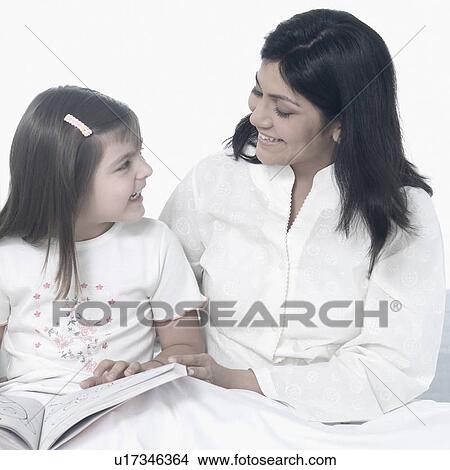 Mid adult woman with her daughter sitting on the bed and smiling View Large Photo Image Picture - Mid adult woman with her daughter sitting on the bed and smiling. Fotosearch