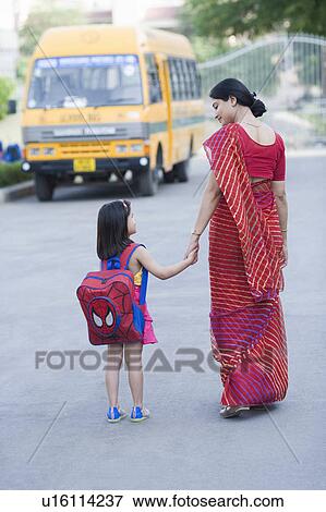 Stock Photo - Rear view of a mid adult woman holding hand of her daughter and walking on the road. Fotosearch