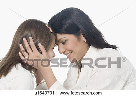 Stock Image - Side profile of a mid adult woman smiling with her daughter. Fotosearch