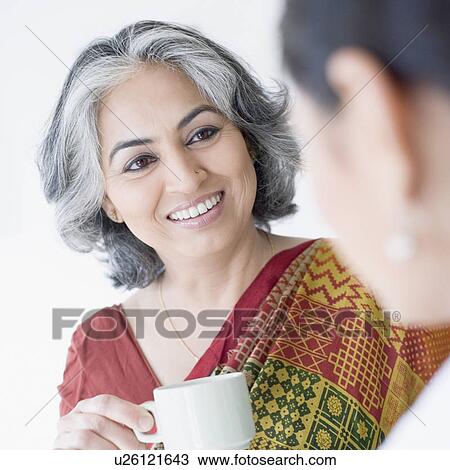 Stock Image - Close-up of a businesswoman holding a cup of tea and talking to her colleague. Fotosearch