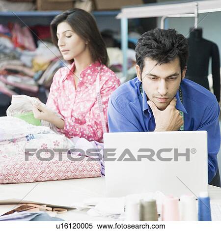 Close-up of a male fashion designer using a laptop with a female fashion designer in the background View Large Photo Image Stock Photography - Close-up of a male fashion designer using a laptop with a female fashion designer in the background. Fotosearch