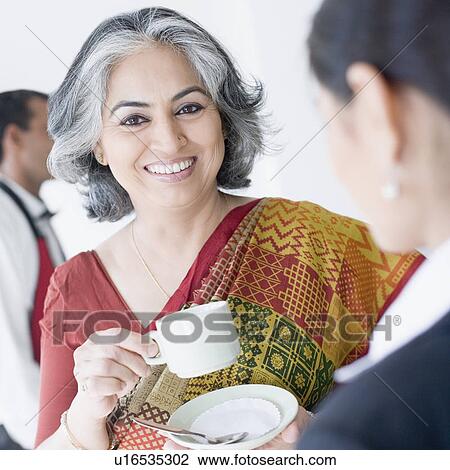 Stock Image - Close-up of two businesswomen holding cups of tea. Fotosearch
