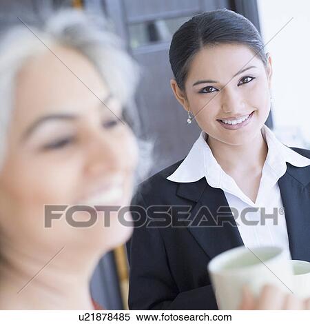 Close-up of two businesswomen holding cups of tea and smiling View Large Photo Image Stock Photography - Close-up of two businesswomen holding cups of tea and smiling. Fotosearch