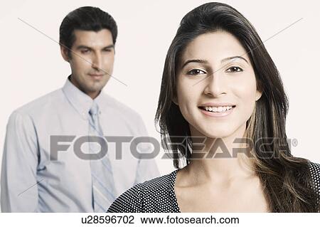 Portrait of a young woman smiling with a young man standing behind her View Large Photo Image Stock Image - Portrait of a young woman smiling with a young man standing behind her. Fotosearch
