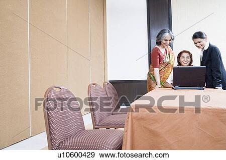 Three businesswomen using a laptop and smiling View Large Photo Image Stock Photo - Three businesswomen using a laptop and smiling. Fotosearch