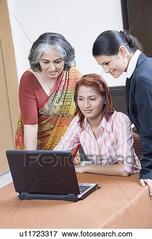 Stock Photo - Three businesswomen using a laptop and smiling. Fotosearch