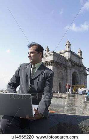 Businessman holding a laptop on his lap with a monument in the background, Gateway of India, Mumbai, Maharashtra, India View Large Photo Image Stock Image - Businessman holding a laptop on his lap with a monument in the background, Gateway of India, Mumbai, Maharashtra, India. Fotosearch