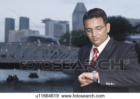Businessman looking at his wristwatch, Singapore View Large Photo Image Stock Photo - Businessman looking at his wristwatch, Singapore. Fotosearch