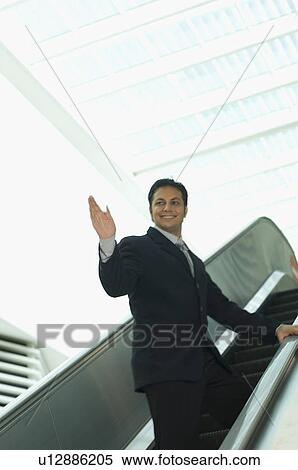 Businessman standing on an escalator and waving his hand View Large Photo Image Stock Photography - Businessman standing on an escalator and waving his hand. Fotosearch
