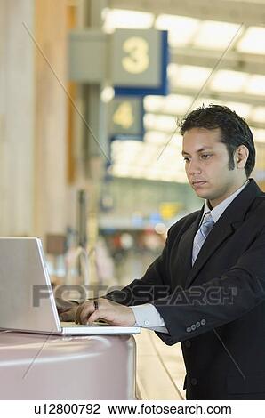 Businessman using a laptop at an airport View Large Photo Image Stock Image - Businessman using a laptop at an airport. Fotosearch