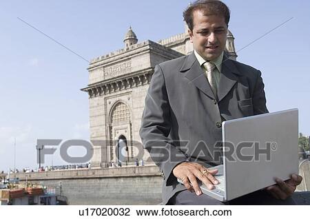 Businessman using a laptop with a monument in the background, Gateway of India, Mumbai, Maharashtra, India View Large Photo Image Stock Image - Businessman using a laptop with a monument in the background, Gateway of India, Mumbai, Maharashtra, India. Fotosearch