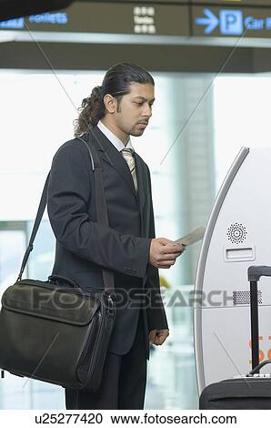 Stock Image - Businessman using express check-in service at an airport. Fotosearch