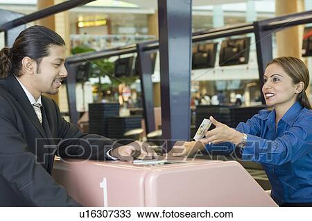 Stock Image - Businessman with an airline check-in attendant sitting at an airport check-in counter. Fotosearch
