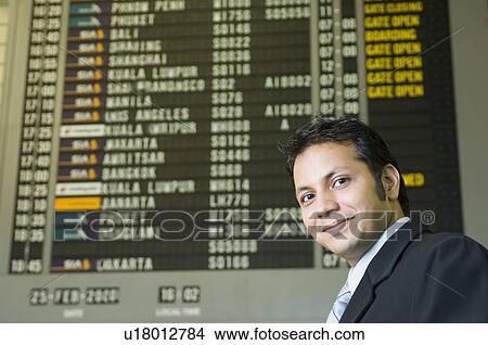 Picture - Portrait of a businessman grinning in front of an arrival departure board. Fotosearch