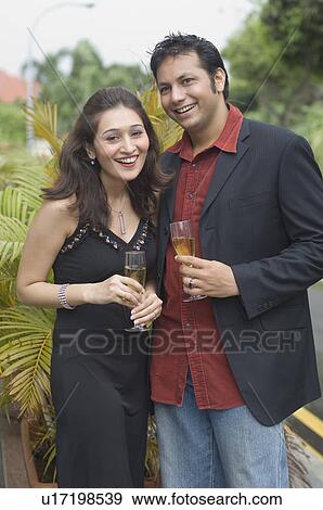 Stock Photo - Portrait of a young couple holding champagne flutes and smiling. Fotosearch