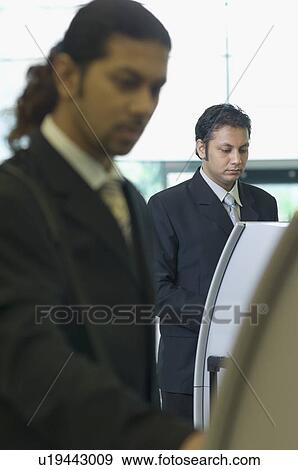 Two businessmen using express check-in service at an airport View Large Photo Image Stock Photo - Two businessmen using express check-in service at an airport. Fotosearch
