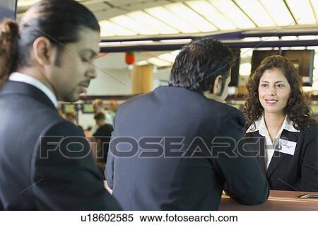 Stock Photography - Two businessmen with an airline check-in attendant at an airport check-in counter. Fotosearch