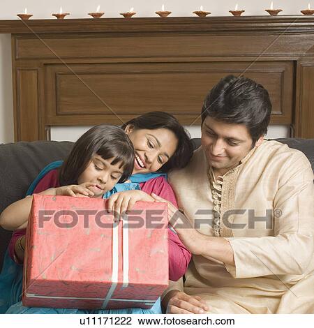 Close-up of a couple and their daughter sitting on a couch with a gift View Large Photo Image Stock Image - Close-up of a couple and their daughter sitting on a couch with a gift. Fotosearch