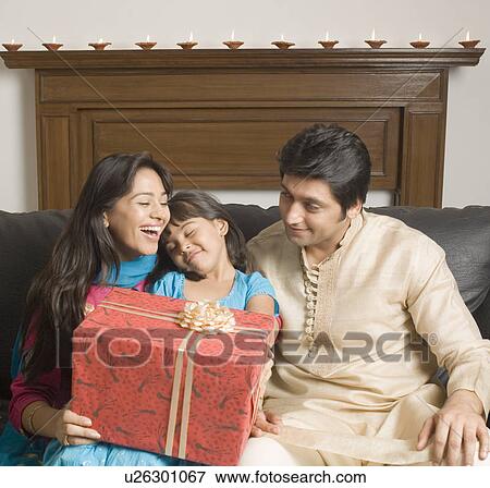 Close-up of a couple and their daughter sitting on a couch with a gift View Large Photo Image Stock Photo - Close-up of a couple and their daughter sitting on a couch with a gift. Fotosearch