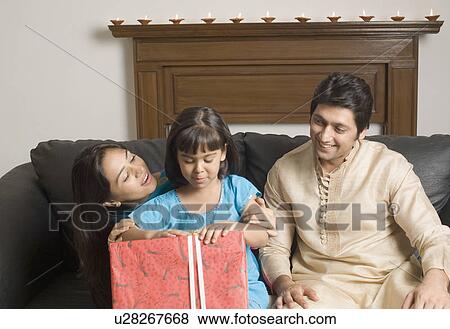 Close-up of a couple and their daughter sitting on a couch with a gift View Large Photo Image Stock Photo - Close-up of a couple and their daughter sitting on a couch with a gift. Fotosearch