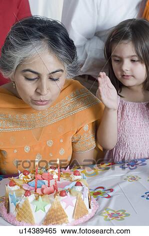 Close-up of a mature woman blowing candles on a birthday cake with her granddaughter standing beside her View Large Photo Image Stock Photography - Close-up of a mature woman blowing candles on a birthday cake with her granddaughter standing beside her. Fotosearch