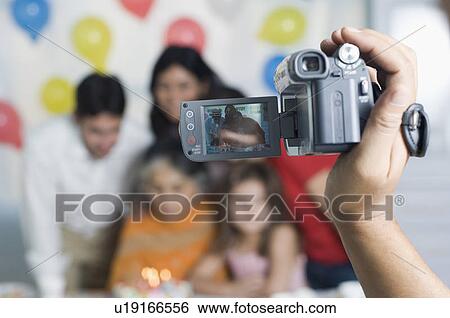 Stock Photograph - Close-up of a person's hand filming a birthday party with a home video camera. Fotosearch